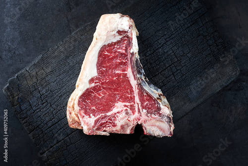 Raw dry aged wagyu t-bone beef steak offered as top view on a rustic charred wooden board with copy space right