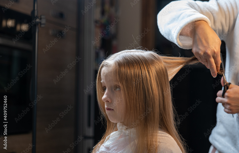 Fototapeta premium hair cutting at home, mom cuts daughter's hair in the kitchen