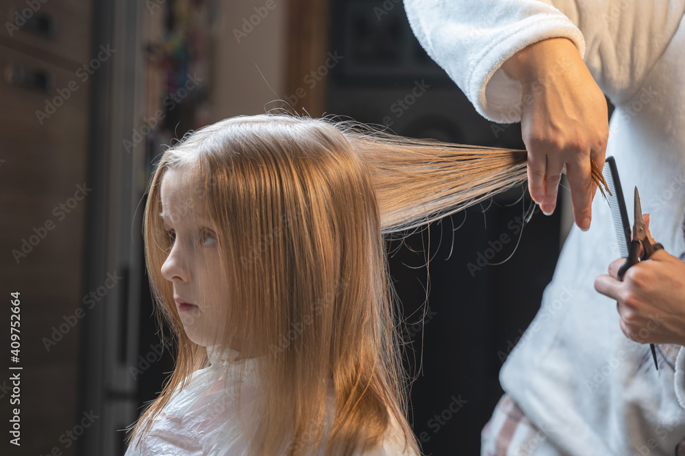 Fototapeta premium hair cutting at home, mom cuts daughter's hair in the kitchen
