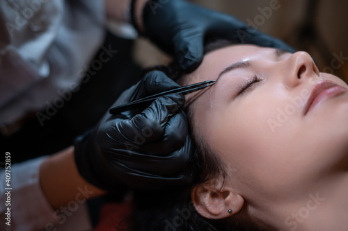 beautiful female at beautician on eyebrows correction procedure with tweezers