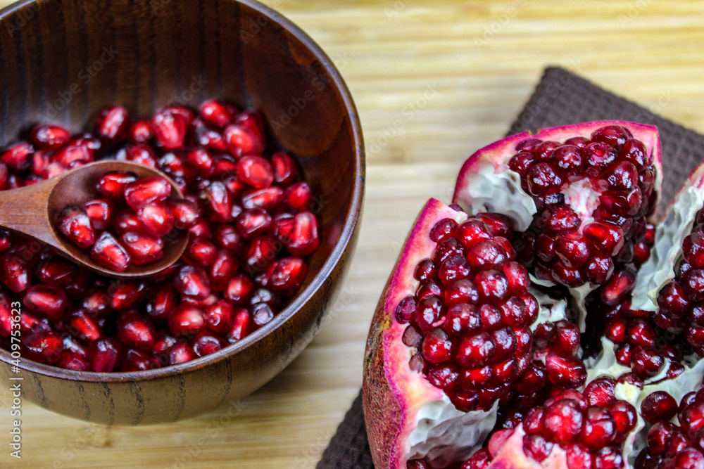 Pomegranate seeds on a wooden spoon in a bowl. Whole ripe pomegranate open on a wooden tray. Red pomegranate fruit seeds in a wooden bowl. Pomegranate seeds on a wooden spoon in a bowl. Whole ripe pomegranate open on a wooden tray. Red pomegranate fruit seeds in a wooden bowl.