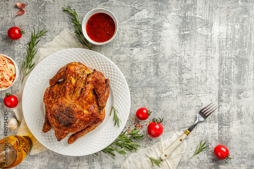 Top view or flat lay of a tasty juicy whole grilled and roasted chicken with golden brown crust, in a white plate served with barbeque sauce, wegetables and salade photo