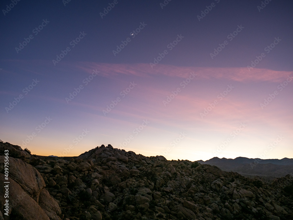 Field of boulders at dusk with sunset sky and crescent moon in Yucca Valley, California near Joshua Tree National Park