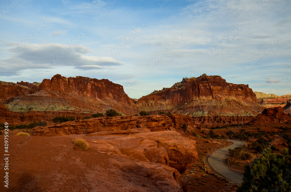 Sunset during golden hour in Southern Utah, sun warming red sandstone, cliffs, mountains, and mesa, and sun