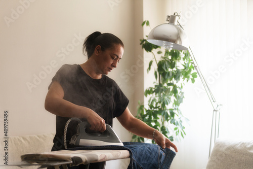 Mujer ama de casa planchando los vaqueros con vapor en el salón de su hogar.