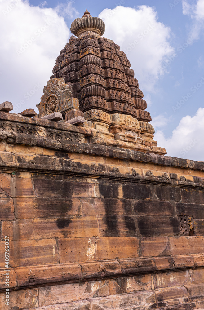 Aihole, Karnataka, India - November 7, 2013: Huchchimalli Gudi or Temple. Closeup portrait of vimanam tower on top under blue cloudscape. All brown stones with black mold patches.