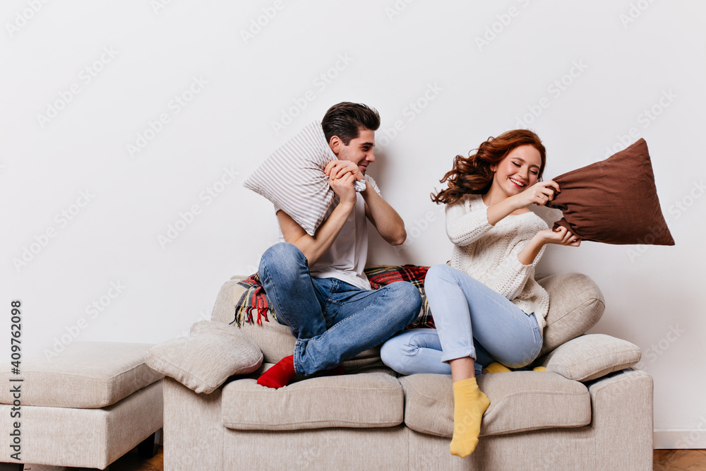 Young people in jeans spending valentine's day at home. Smiling friends posing during pillow fight.