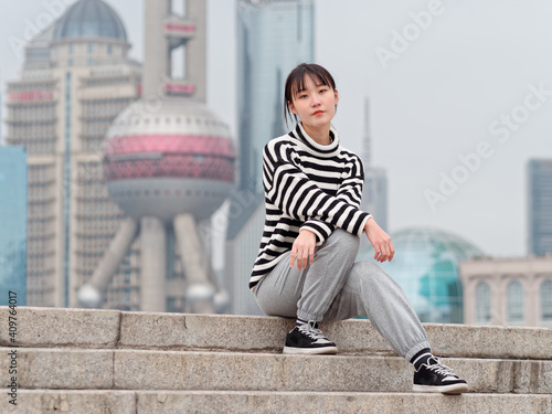 Portrait of Chinese young woman sitting on steps with Shanghai landmarks background.