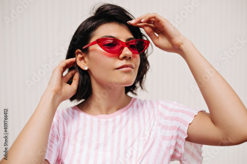Curious young woman looking away isolated on textured background. Appealing caucasian girl in summer outfit posing in sunglasses.