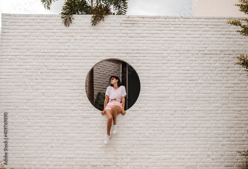 Outdoor shot of good-humoured stylish girl on bricked wall. Gorgeous female model posing on street.