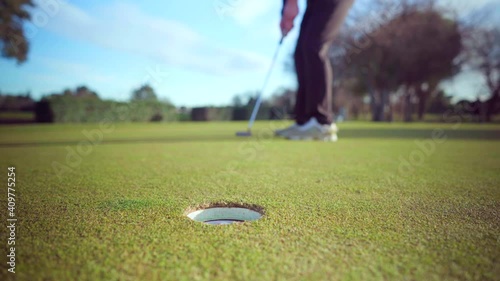 Succesful putting shot by golfer on the putting-green of a golf course on a sunny day, close-up on the hole