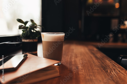 Cup of coffee, notebook, phone at table in cafe. Blurred background