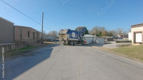 Garbage truck lifting and emptying a trash dumpster then leaves the alley photo