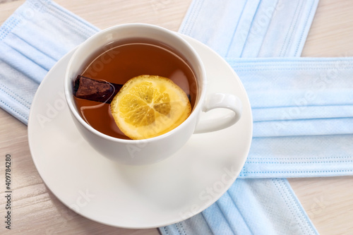 A cup of tea with a slice of lemon and cinnamon is on the medical mask. The concept of prevention against viruses
