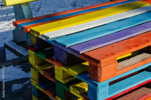 Stack of colorful wooden pallets outside.