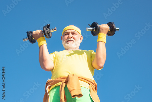 Senior fitness man training with dumbbells isolated on blue background. Senior man in gym working out with weights. Senior man lifting weights.