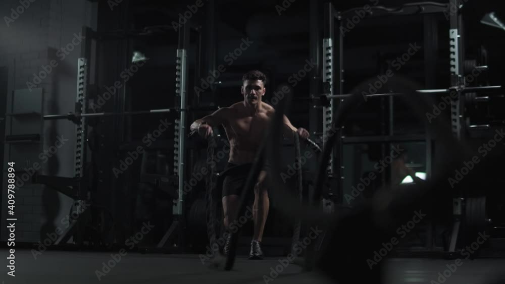 Athletic man performs exercises with battle ropes, endurance training in the gym, cinematic light, 4k slow motion. Athletic man performs exercises with battle ropes, endurance training in the gym, cinematic light, 4k slow motion.