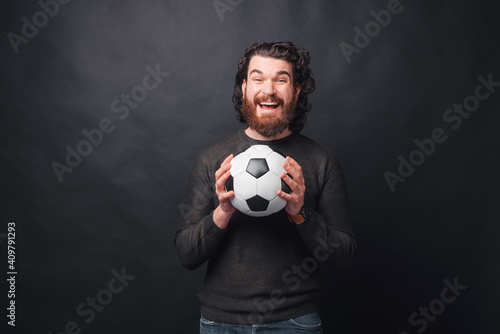 A man is holding excited a soccer ball near a black wall .