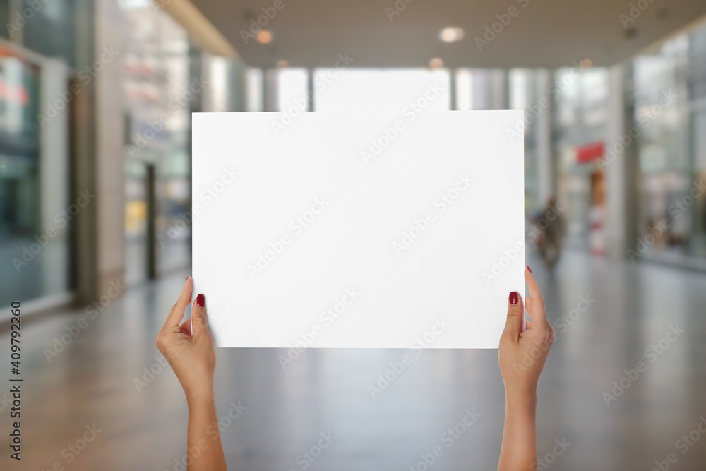 Female hands with blank poster in hall of shopping mall Female hands with blank poster in hall of shopping mall