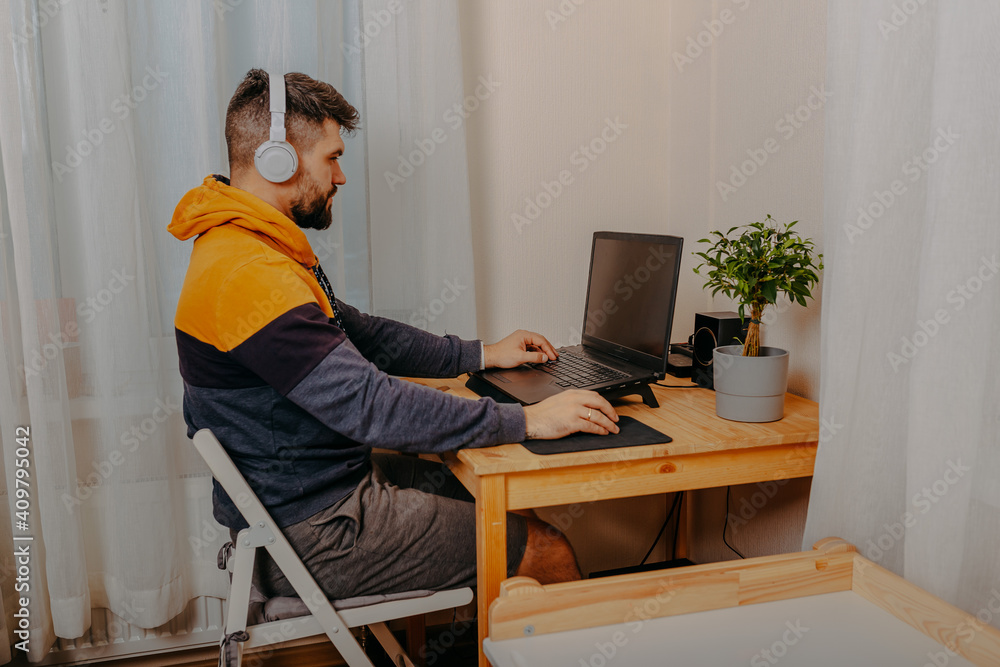 Young man playing computer games in white headphones. Gamer at home. Man working on computer at home. Young man playing computer games in white headphones. Gamer at home. Man working on computer at home.