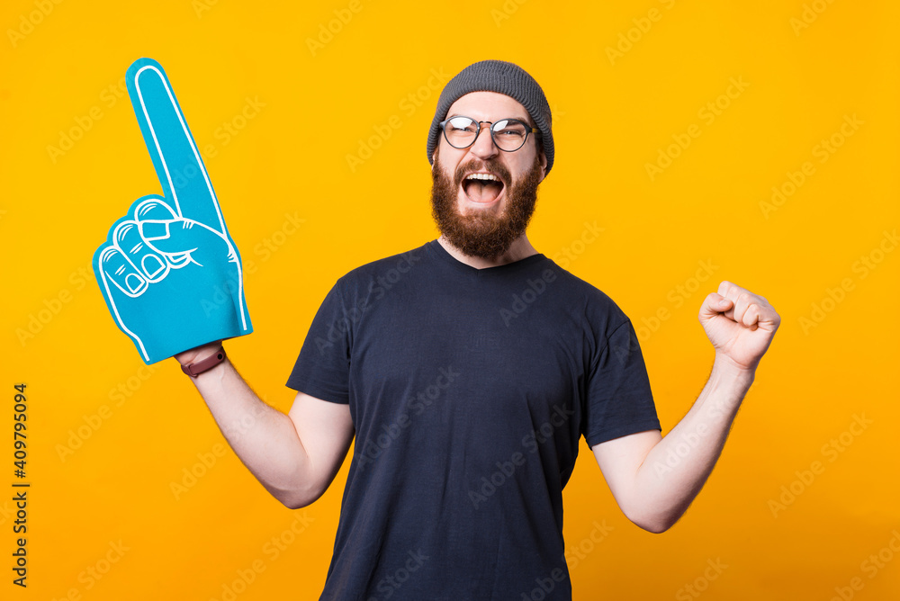 Photo of a a young man screaming of happiness with a fan glove on because his football team won . Photo of a a young man screaming of happiness with a fan glove on because his football team won .