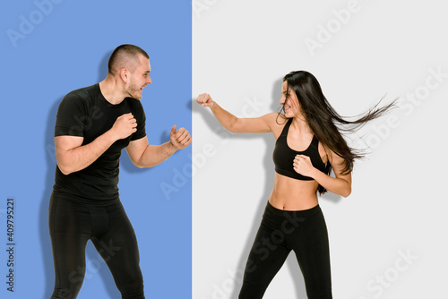 Portrait of young athletic female kickboxer training with coach on a split background of blue and light gray