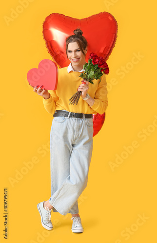 Young transgender woman with flowers and gift on color background. Valentine's Day celebration