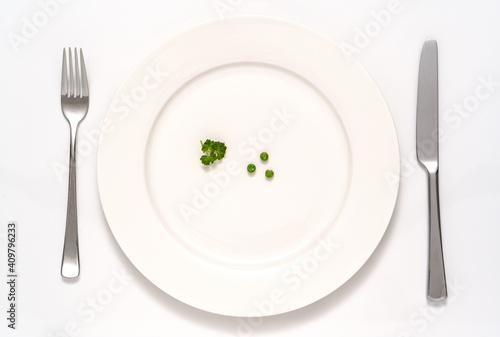 Drei Erbsen und etwas Petersilie auf einem weissen Teller mit Messer und Gabel