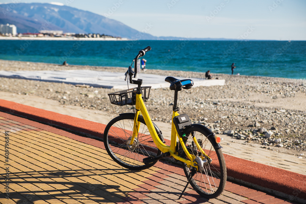 Obraz premium Yellow bike leaning on the pavement blue sea background