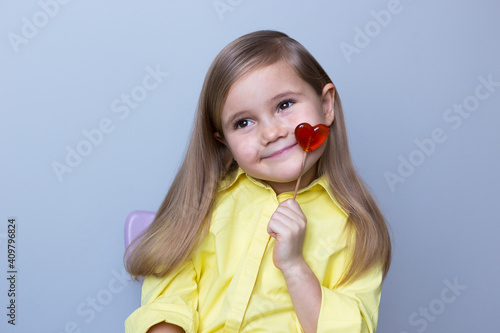 valentine's day caucasian child holding a lollipop heart over grey background.Donation,heart health,world heart day, world health day,world mental health day.Health and heart concept.