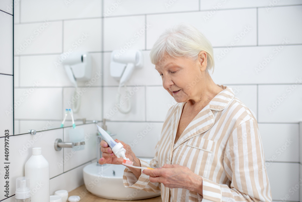 Elderly woman squeezing toothpaste an a toothbrush Elderly woman squeezing toothpaste an a toothbrush