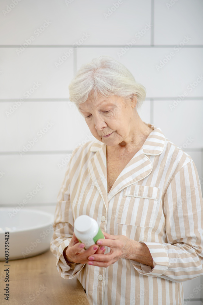 Short-haired old lady holding a bottle with vitamins in her hands Short-haired old lady holding a bottle with vitamins in her hands
