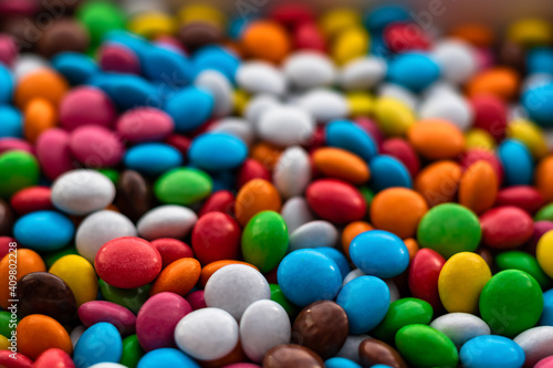 Lots of multicolored round dragee candies fill the entire frame. Focus on the foreground. The background fades into bokeh. Background from multicolored food.