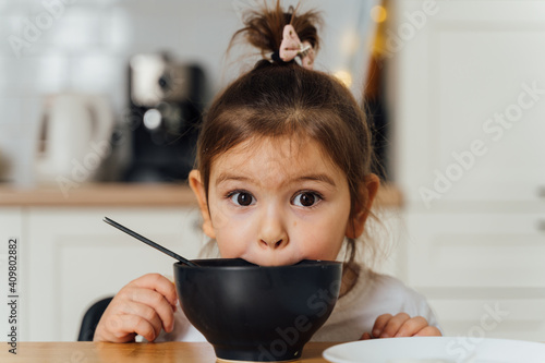 toddler girl picky eater at home kitchen. learning o eat with spoon. bad table manners of kid