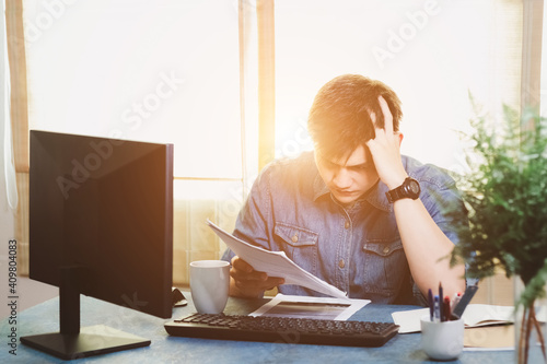 Young Asian men are stressed out in business office. Looking at expense bill and the other hand on head, thinking about finding money to pay credit card debt and all bills. Concept financial problems.