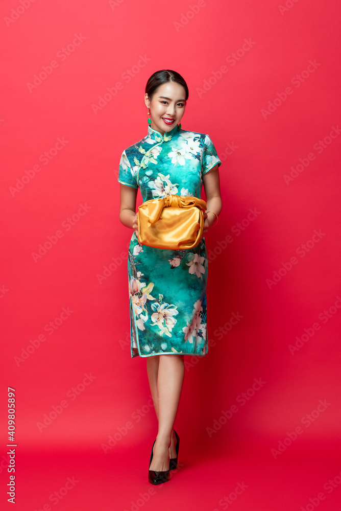 Happy smiling Asian woman in traditional costume giving gold gift box in red isolated studio background for Chinese new year concepts Happy smiling Asian woman in traditional costume giving gold gift box in red isolated studio background for Chinese new year concepts