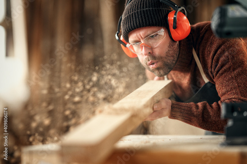 Leinwand Poster Carpenter blowing sawdust from wooden plank