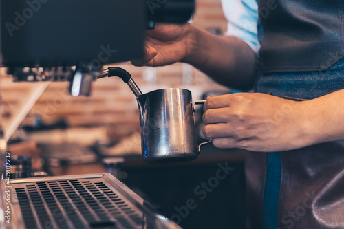 Barista heats milk steam for making lattes at coffee shop.