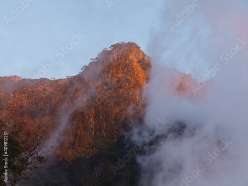 Mountain peak with clouds rising lke smoke in the dusk