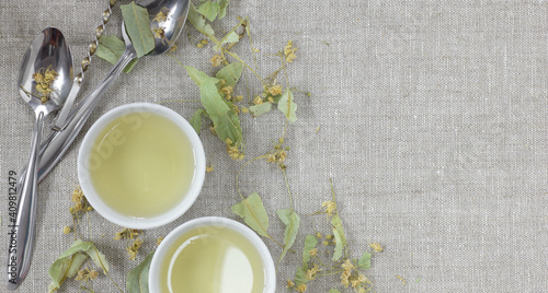 Dried lime-blossoms from above on linen textile with lime leaf flower buds neaby and cups with tea, overhead top view, flat lay, closeup, copy space, herbal tea nad naturopathy concept