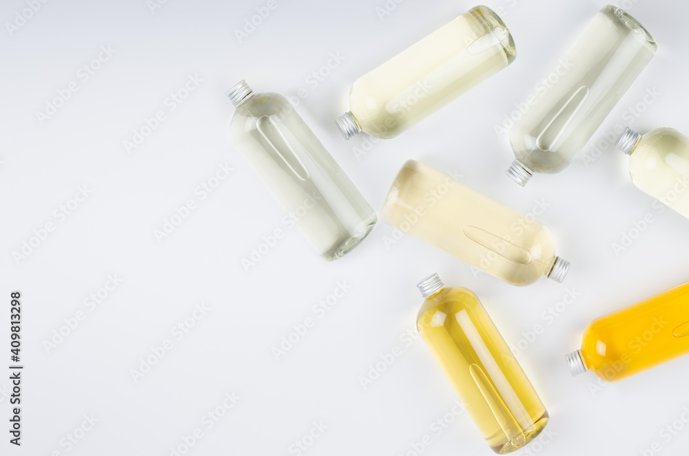 Abstract cosmetic border of lying bottles with different pale colors liquid, silver cap on white background, top view, copy space. Abstract cosmetic border of lying bottles with different pale colors liquid, silver cap on white background, top view, copy space.