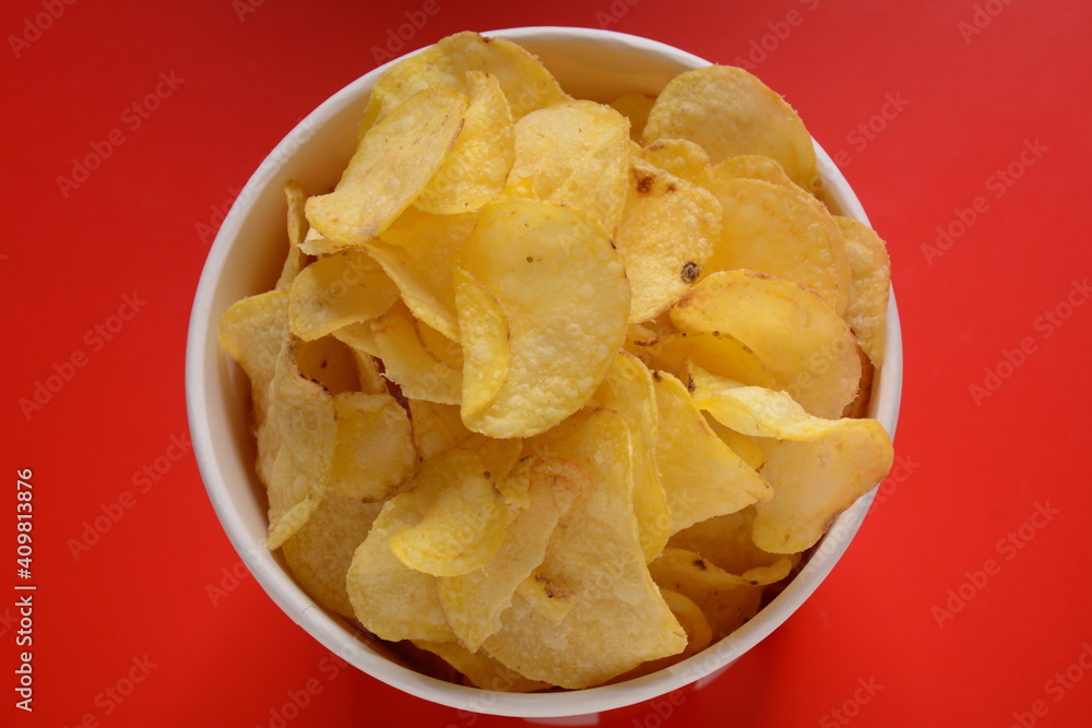 Crispy potato chips in bowl on red background Crispy potato chips in bowl on red background