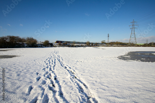 Tracks in a snowy field leading to railway line © simonXT2