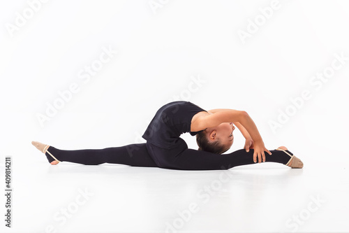 Girl gymnast smiling and warming up in a black sports uniform on a white background. Activity. Exercise
