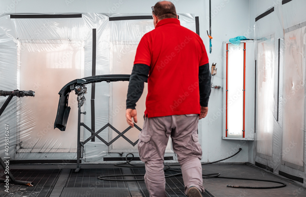 A professional mechanic working in a paint chamber during the coating process of a damaged vehicle. Airbrush technology, high-pressure painting, restyling, automotive wrapping service. A professional mechanic working in a paint chamber during the coating process of a damaged vehicle. Airbrush technology, high-pressure painting, restyling, automotive wrapping service.