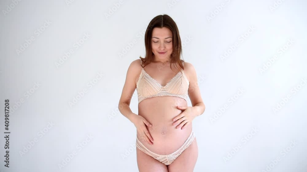 Pregnant woman in underwear on a white background posing and smiling. Young mother expecting a baby enjoying her pregnancy at home. Pretty pregnant woman wearing underwear looking at mirror. Pregnant woman in underwear on a white background posing and smiling. Young mother expecting a baby enjoying her pregnancy at home. Pretty pregnant woman wearing underwear looking at mirror.