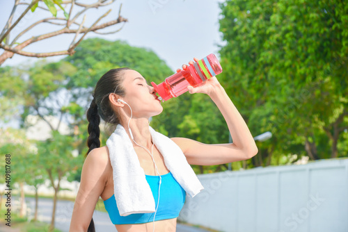 Beautiful asian runner drinking water from bottle in park.