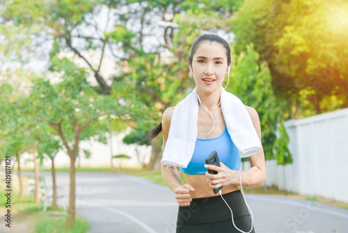 Beautiful asian woman in sportswear listening to music on earphones while running outdoors in the city.