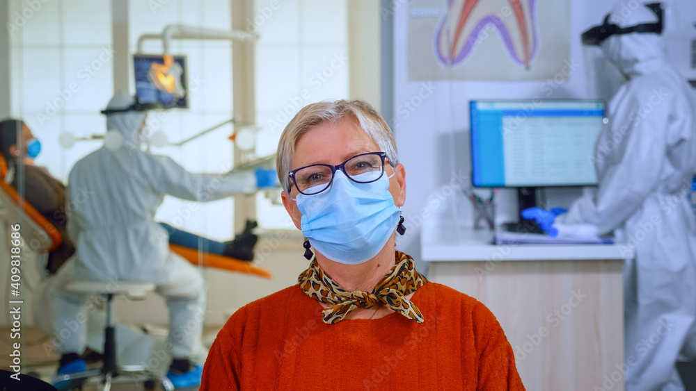Portrait of retired patient in dental office looking on camera wearing face mask sitting on chair in waiting room clinic while doctor working. Concept of new normal dentist visit in coronavirus Portrait of retired patient in dental office looking on camera wearing face mask sitting on chair in waiting room clinic while doctor working. Concept of new normal dentist visit in coronavirus