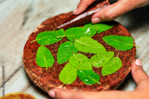 Hindu Religious Ritual. Hindu Puja ritual preparation background. Closeup of sandalwood stick or chandan with grinding stone and holy basil or tulsi leaves. Ritual for Saraswati Lakshmi Durga puja.